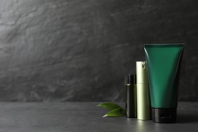 Photo of Facial cream and other men's cosmetic with green leaves on grey stone table. Mockup for design