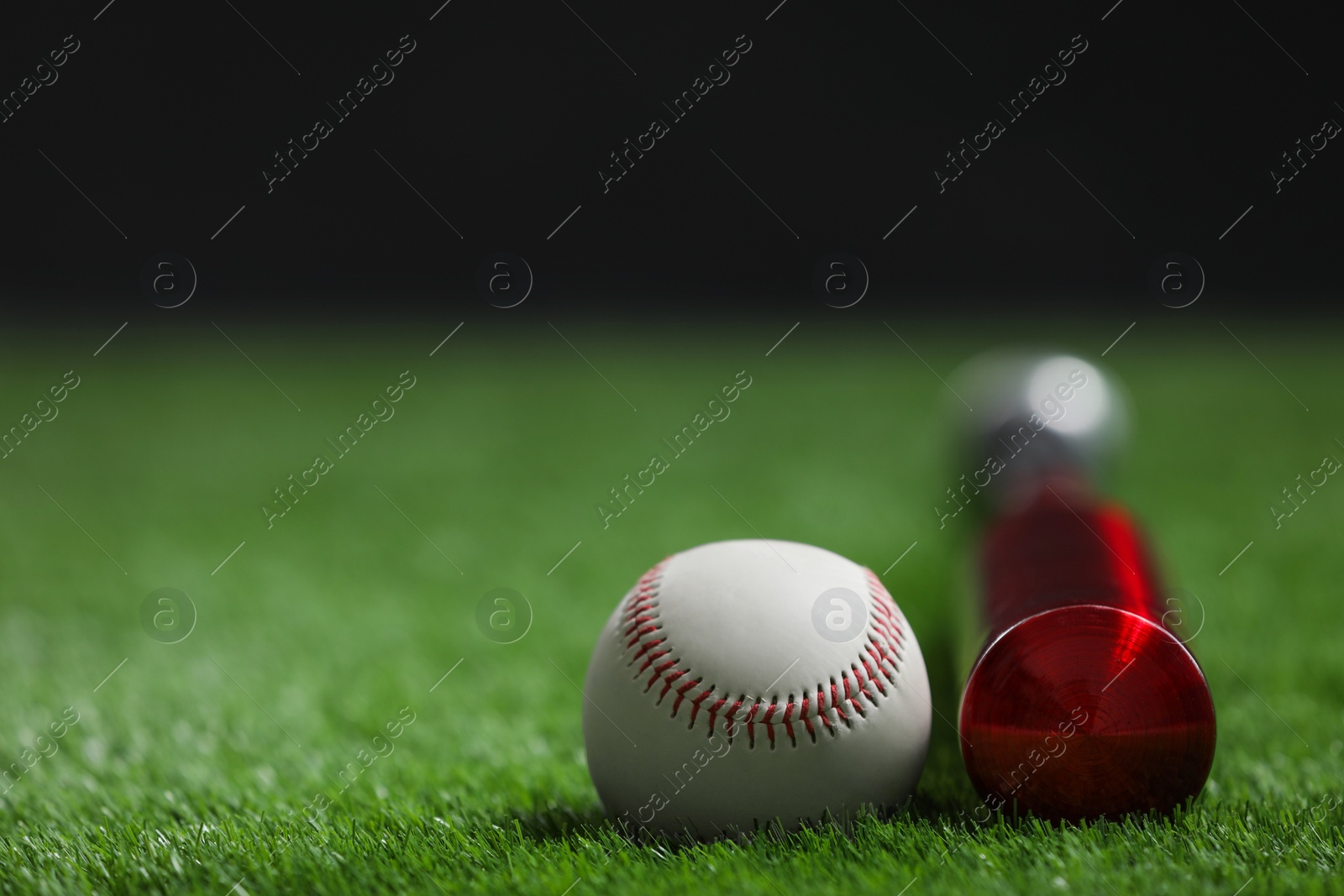 Photo of Baseball bat and ball on green grass against dark background, closeup. Space for text
