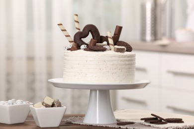 Photo of Delicious cake decorated with sweets on wooden table in kitchen