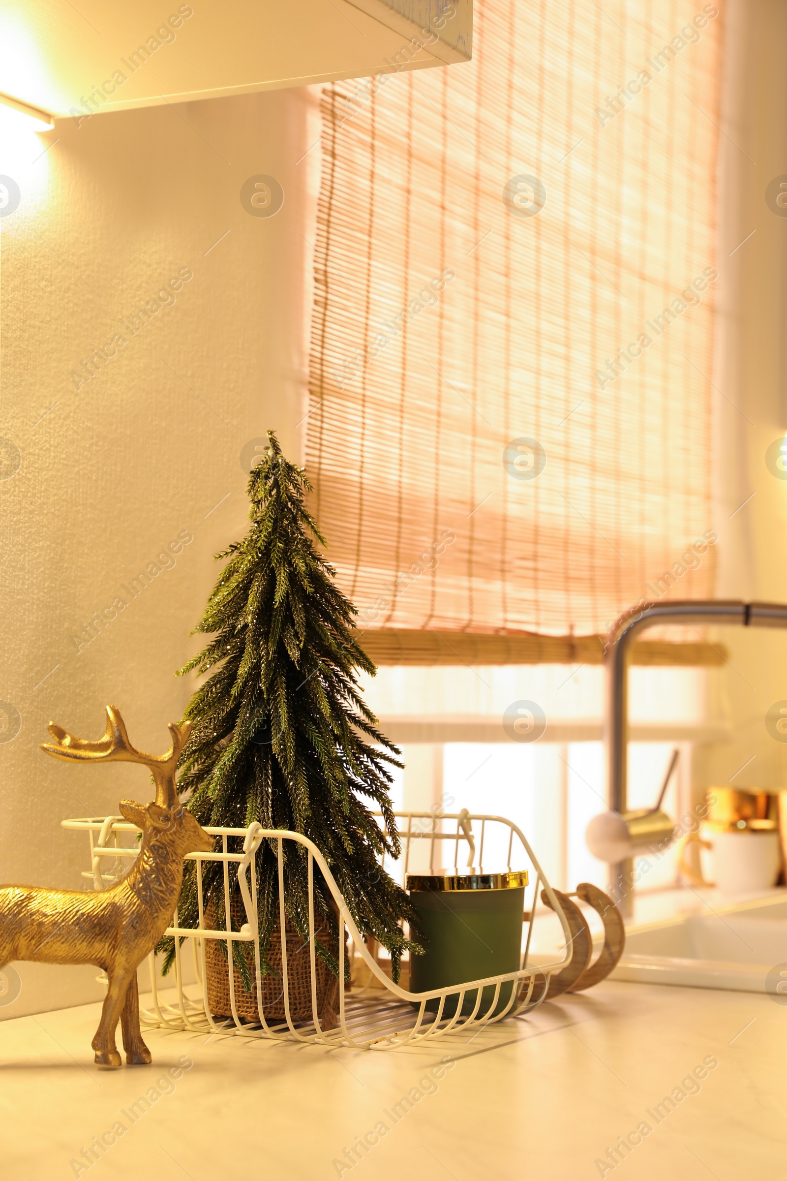 Photo of Little Christmas tree, candle and decorative reindeer on countertop in kitchen