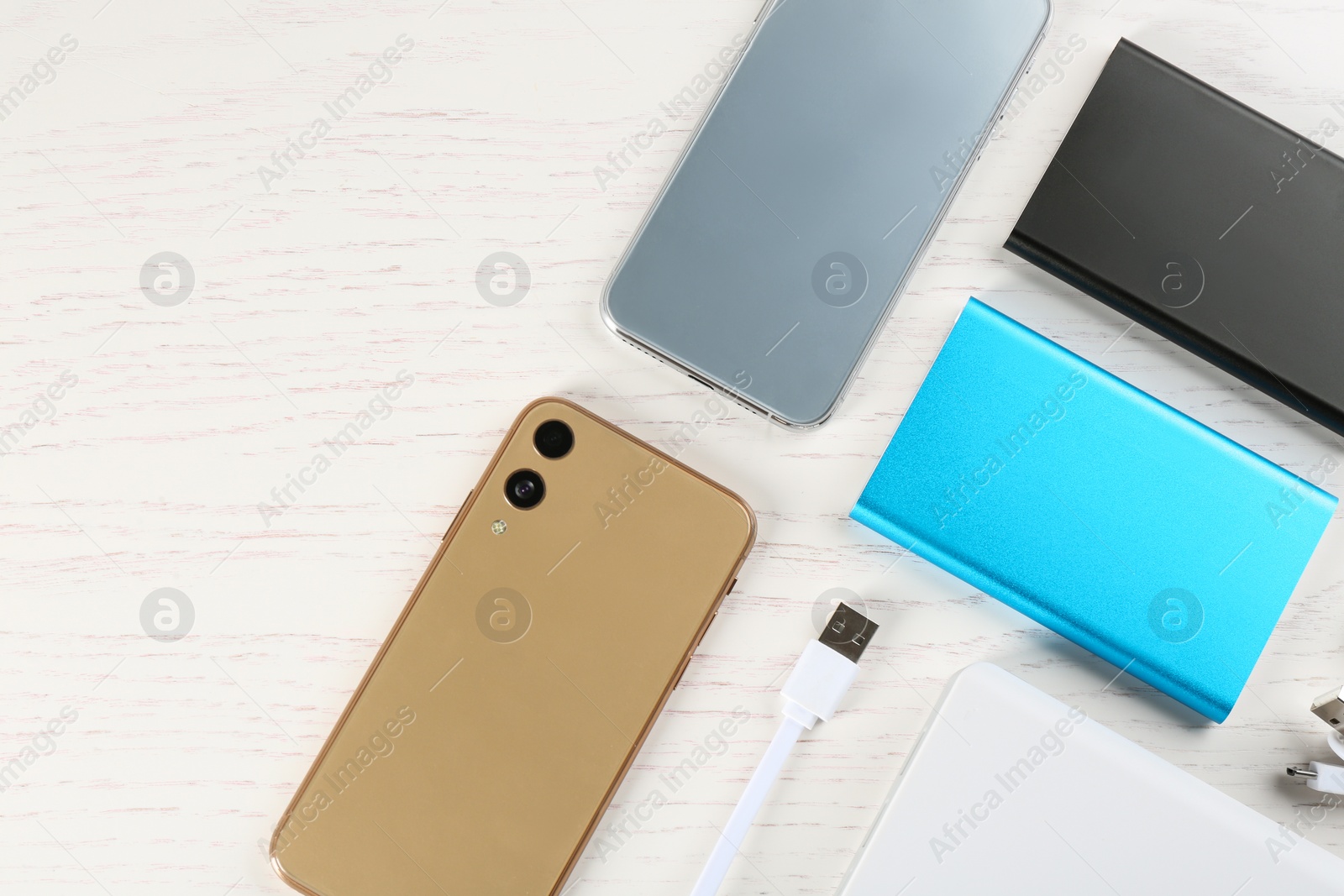 Photo of Flat lay composition with mobile phones and portable chargers on white wooden background
