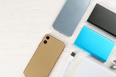 Photo of Flat lay composition with mobile phones and portable chargers on white wooden background