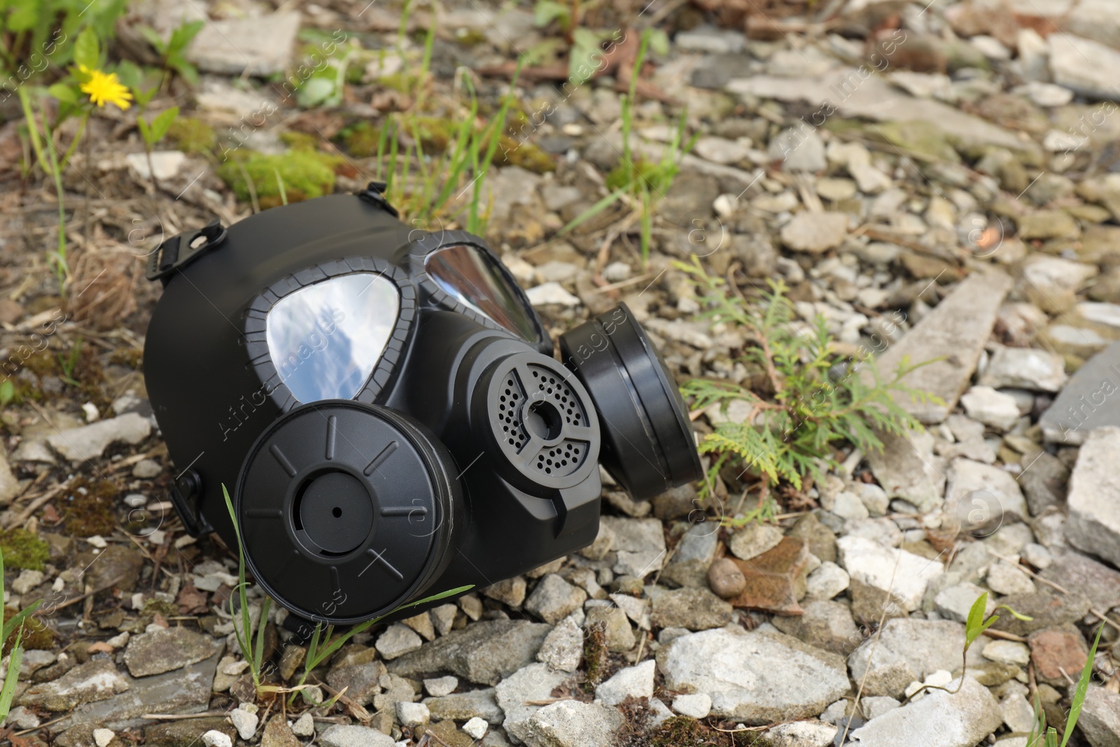 Photo of One gas mask on ground with stones outdoors. Space for text