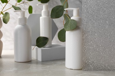 Different face cleansing products and eucalyptus leaves on light grey table