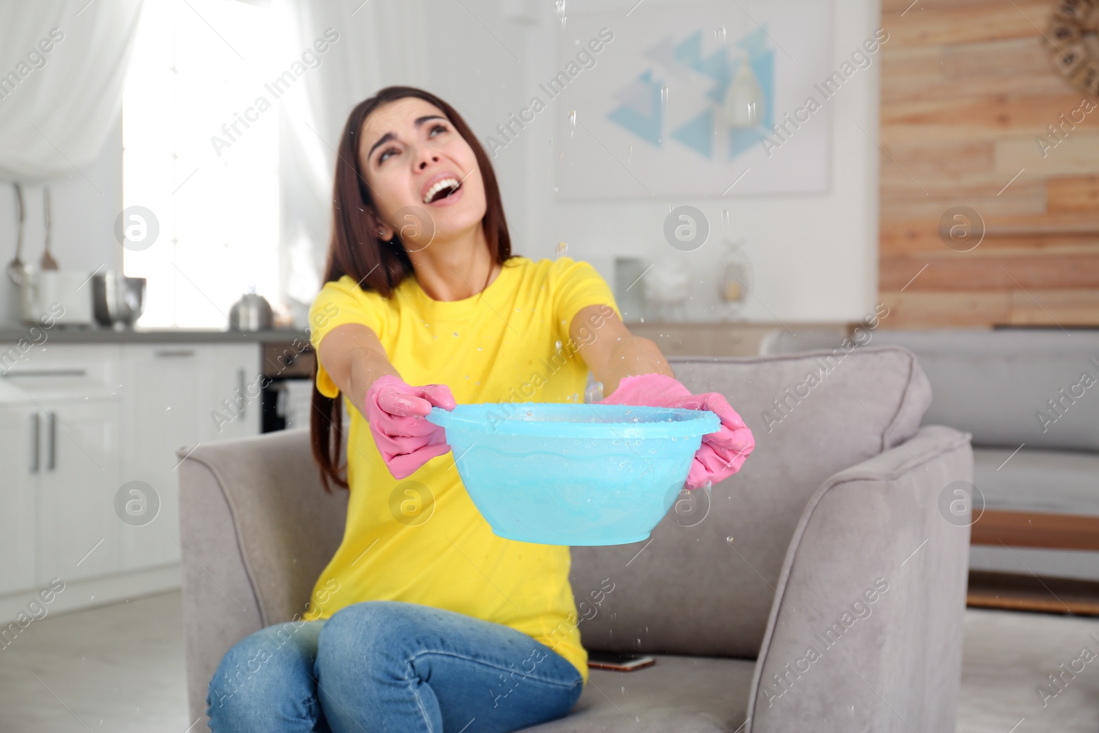 Photo of Woman collecting water leaking from ceiling at home. Time to call plumber