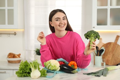 Woman with broccoli and string bag of fresh vegetables at light marble table in kitchen