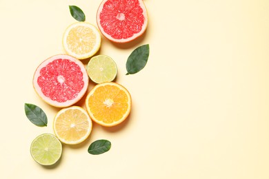 Photo of Different cut citrus fruits and leaves on beige table, flat lay. Space for text