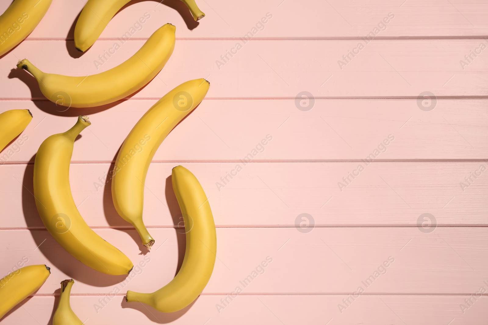Photo of Ripe yellow bananas on light pink wooden table, flat lay. Space for text