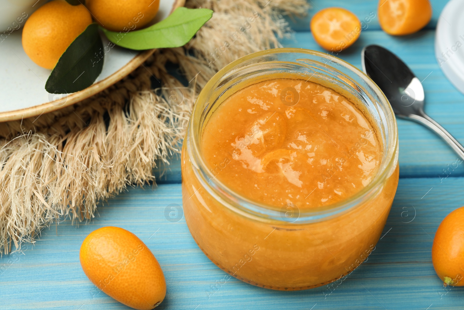 Photo of Delicious kumquat jam in jar on light blue wooden table