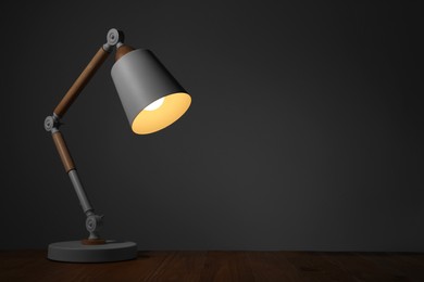 Photo of Stylish modern desk lamp on wooden table at night, space for text