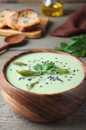 Photo of Bowl of delicious asparagus soup on wooden table, closeup