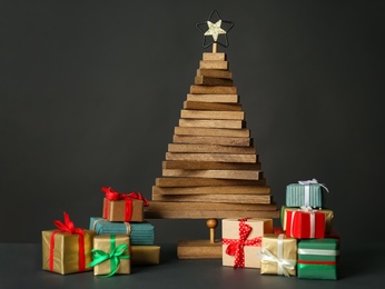Photo of Decorative wooden Christmas tree with gift boxes on dark background, space for text