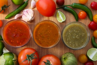 Photo of Tasty salsa sauces and ingredients on wooden table, flat lay