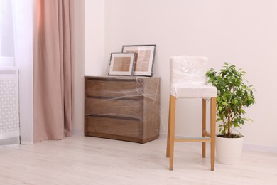 Photo of Picture frames, chair and chest of drawers wrapped in stretch film indoors