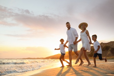 Happy family running on sandy beach near sea at sunset