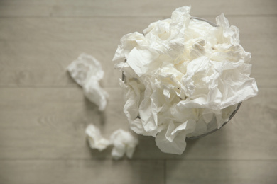 Used paper tissues and trash can on wooden floor, flat lay