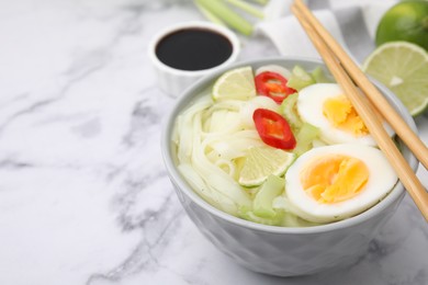 Bowl of delicious rice noodle soup with celery and egg on white marble table, closeup. Space for text