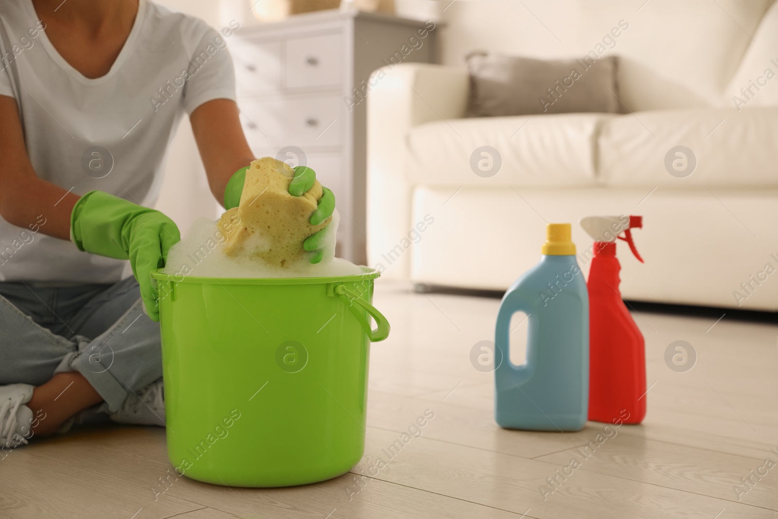 Photo of Woman holding sponge with foam over bucket indoors, closeup. Cleaning supplies