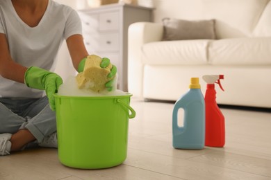 Photo of Woman holding sponge with foam over bucket indoors, closeup. Cleaning supplies