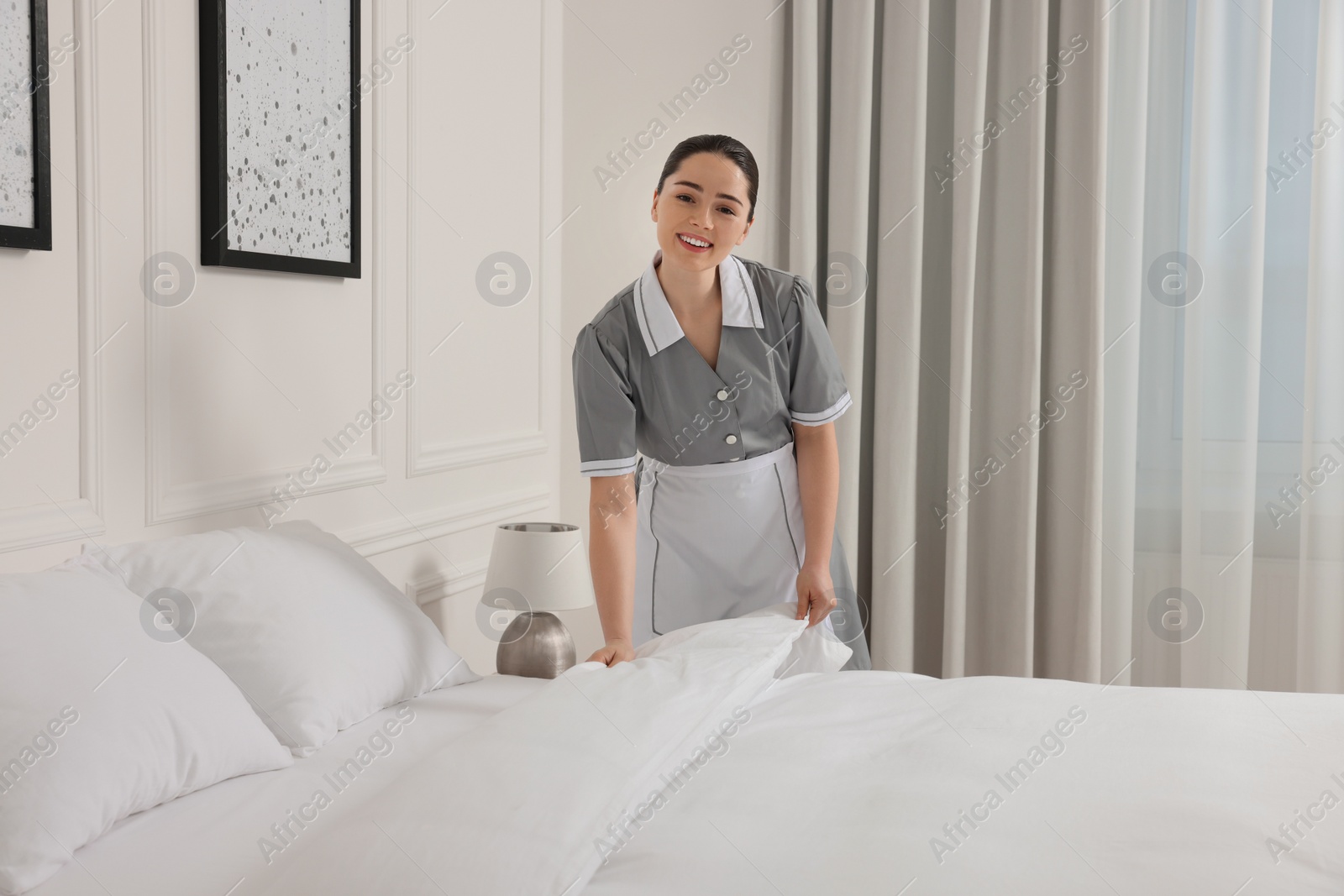 Photo of Young maid making bed in hotel room