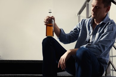 Photo of Addicted man with alcoholic drink on stairs indoors. Space for text