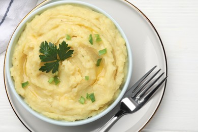 Photo of Bowl of tasty mashed potatoes with parsley and green onion served on white wooden table, top view