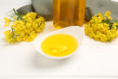 Photo of Rapeseed oil in gravy boat and beautiful yellow flowers on white wooden table