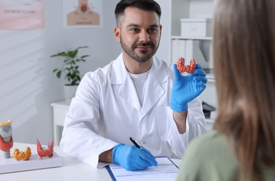 Endocrinologist showing thyroid gland model to patient at table in hospital