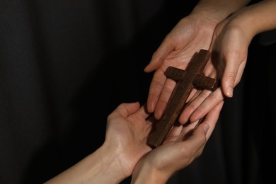 Easter - celebration of Jesus resurrection. Women holding wooden cross on dark background, closeup. Space for text