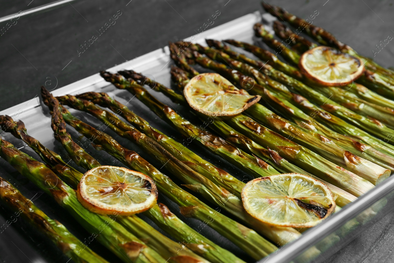 Photo of Oven baked asparagus with lemon slices in glass dish on table, closeup