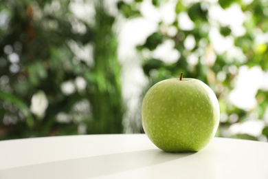 Fresh ripe green apple on white table against blurred background. Space for text