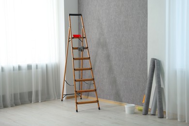Photo of Wallpaper rolls, bucket with glue and wooden ladder in room