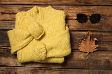 Photo of Warm sweater, sunglasses and dry leaf on wooden background, flat lay. Autumn season