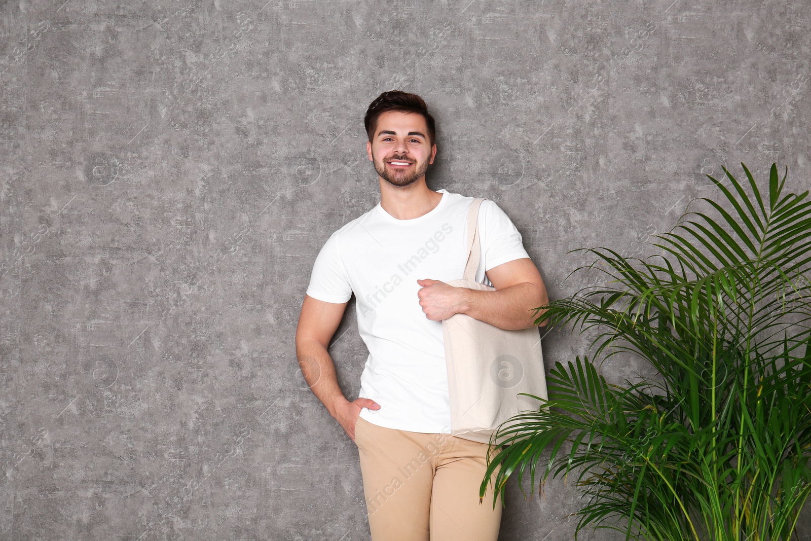 Photo of Portrait of young man with eco bag at indoor palm plant near grey wall