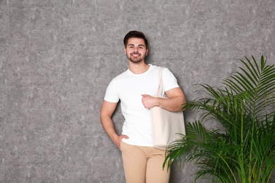 Portrait of young man with eco bag at indoor palm plant near grey wall