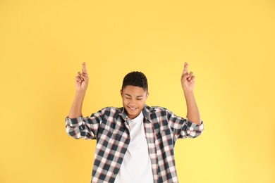 Photo of African-American teenage boy crossing his fingers on color background