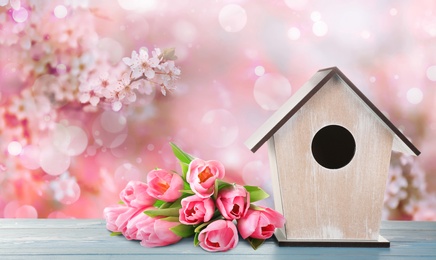 Image of Beautiful bird house and spring flowers on wooden table outdoors