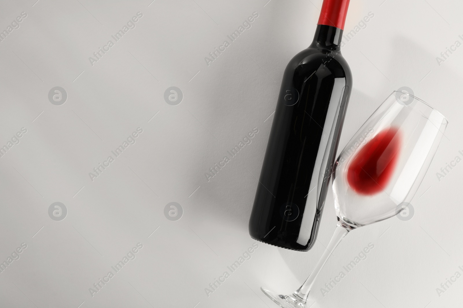 Photo of Bottle of expensive red wine and wineglass on light grey background, top view. Space for text