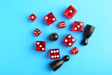 Photo of Many red dices and color game pieces on light blue background, flat lay