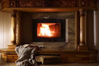 Photo of Blanket, books and firewood near fireplace at home