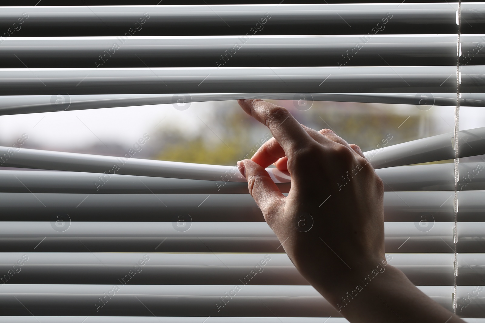 Photo of Woman separating slats of white blinds indoors, closeup