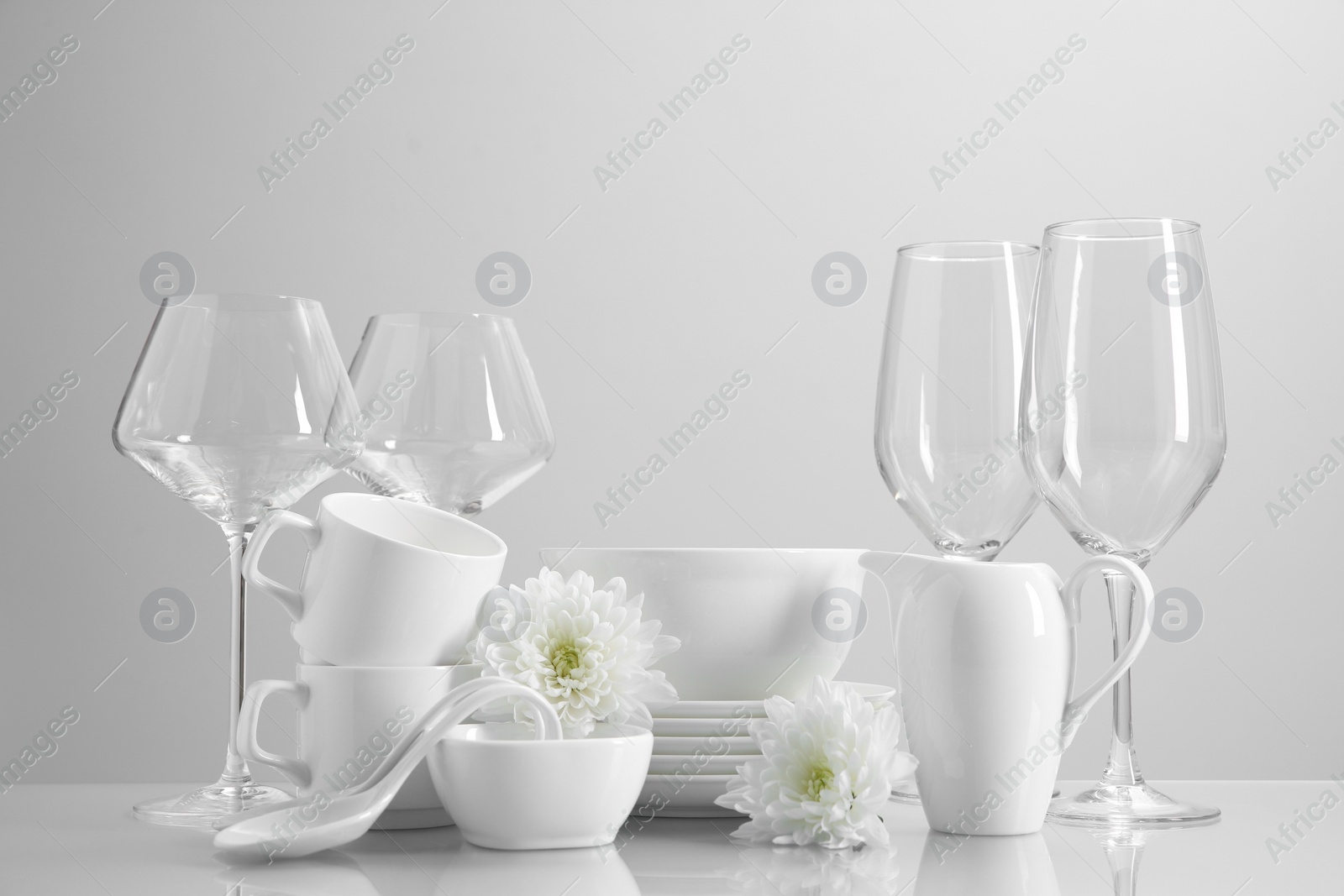 Photo of Set of many clean dishware, flowers and glasses on light table