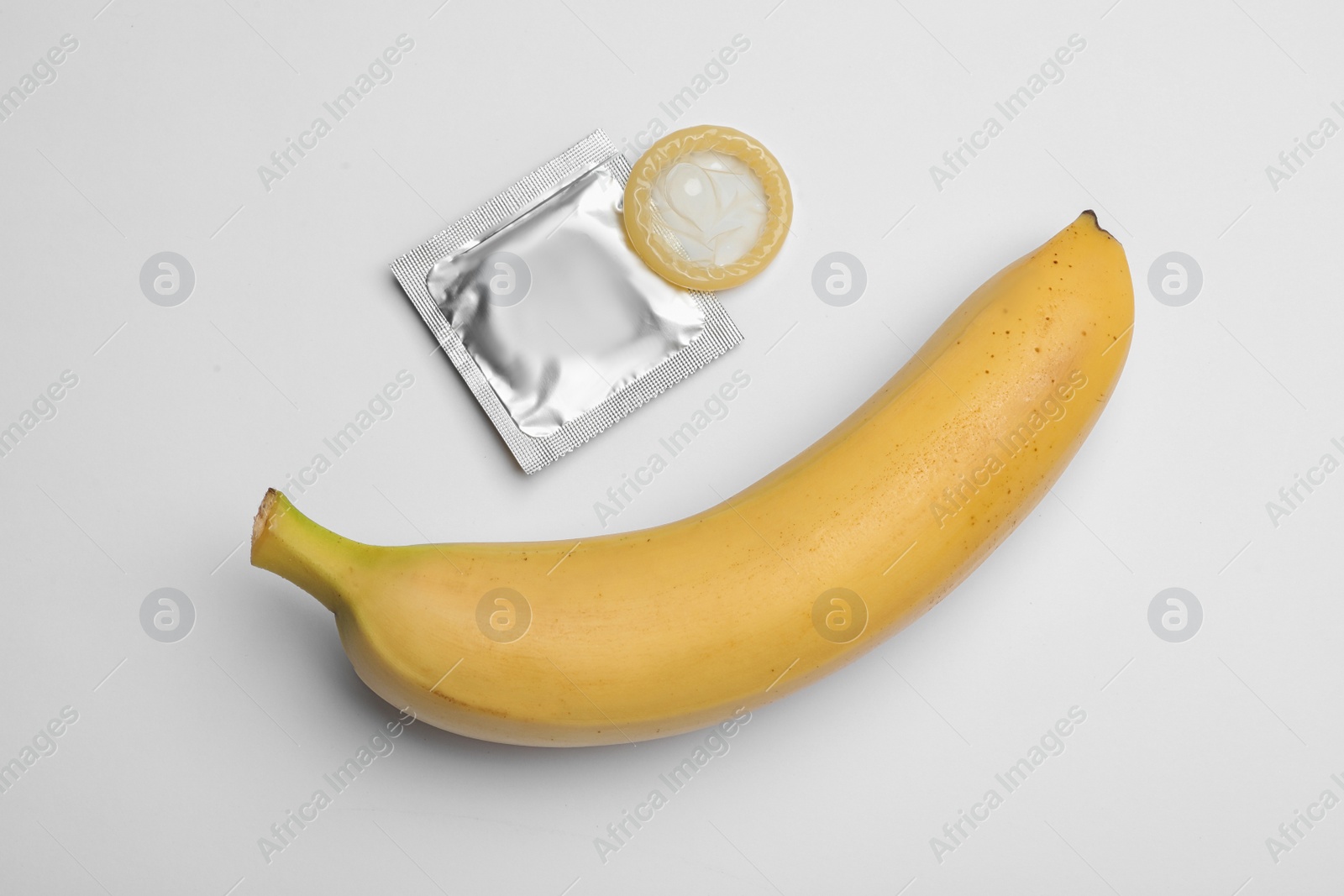 Photo of Condom and banana on white background, top view. Safe sex