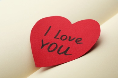 Photo of Paper heart with words I LOVE YOU on open notebook, closeup