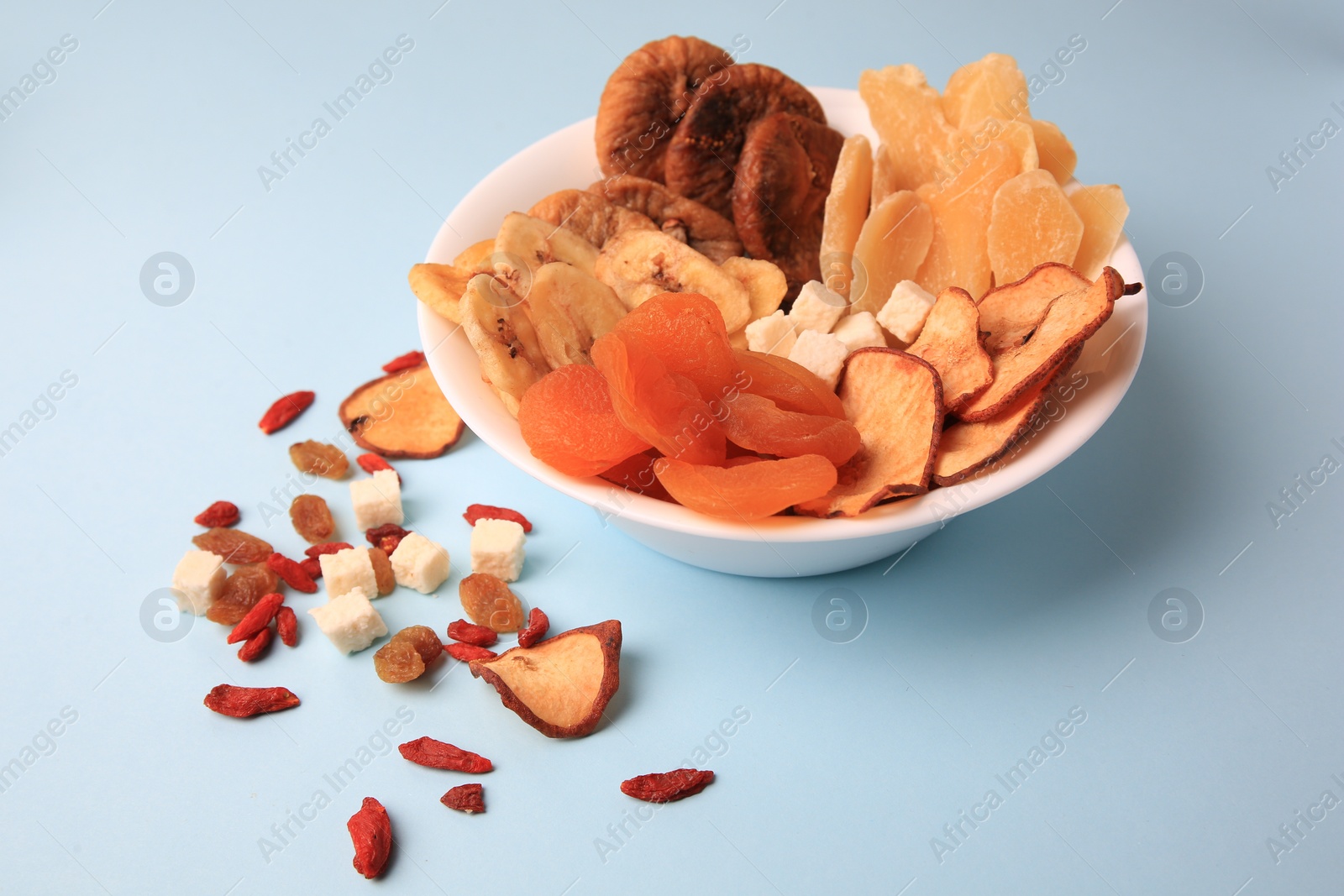 Photo of Bowl with different dried fruits on light blue background