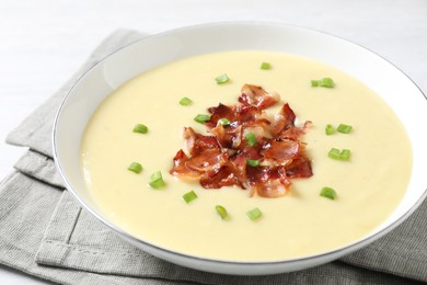 Tasty potato soup with bacon and green onion in bowl on white table