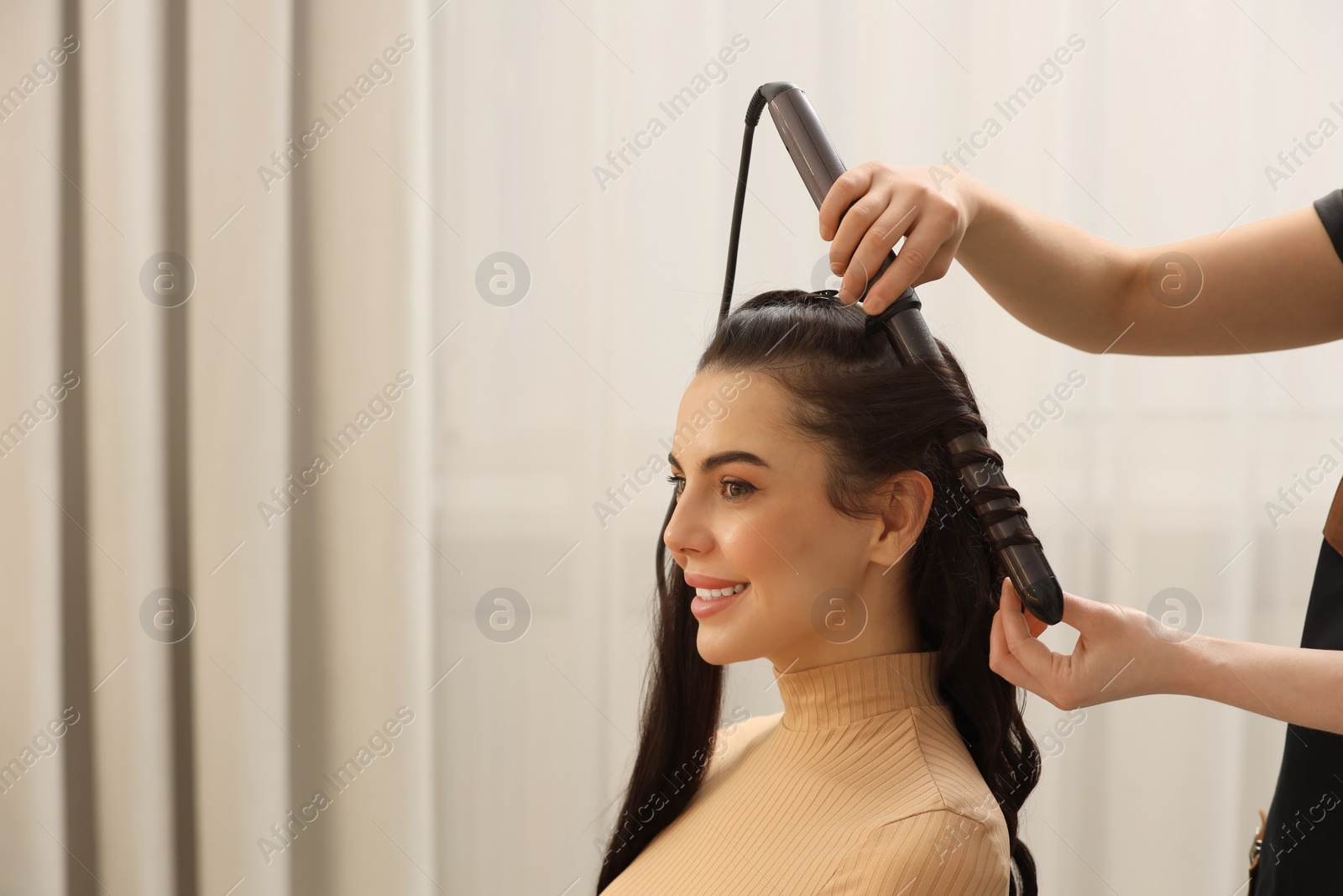 Photo of Hair styling. Hairdresser curling woman's hair in salon, closeup. Space for text