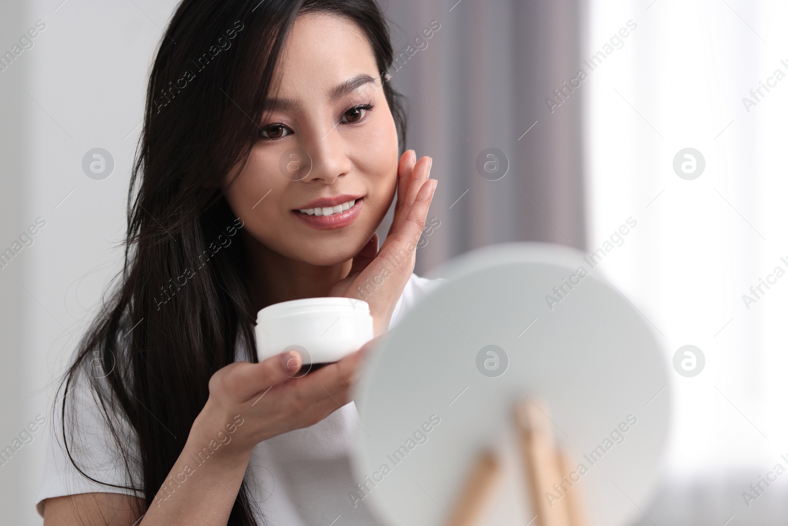 Photo of Happy woman applying face cream at home, space for text