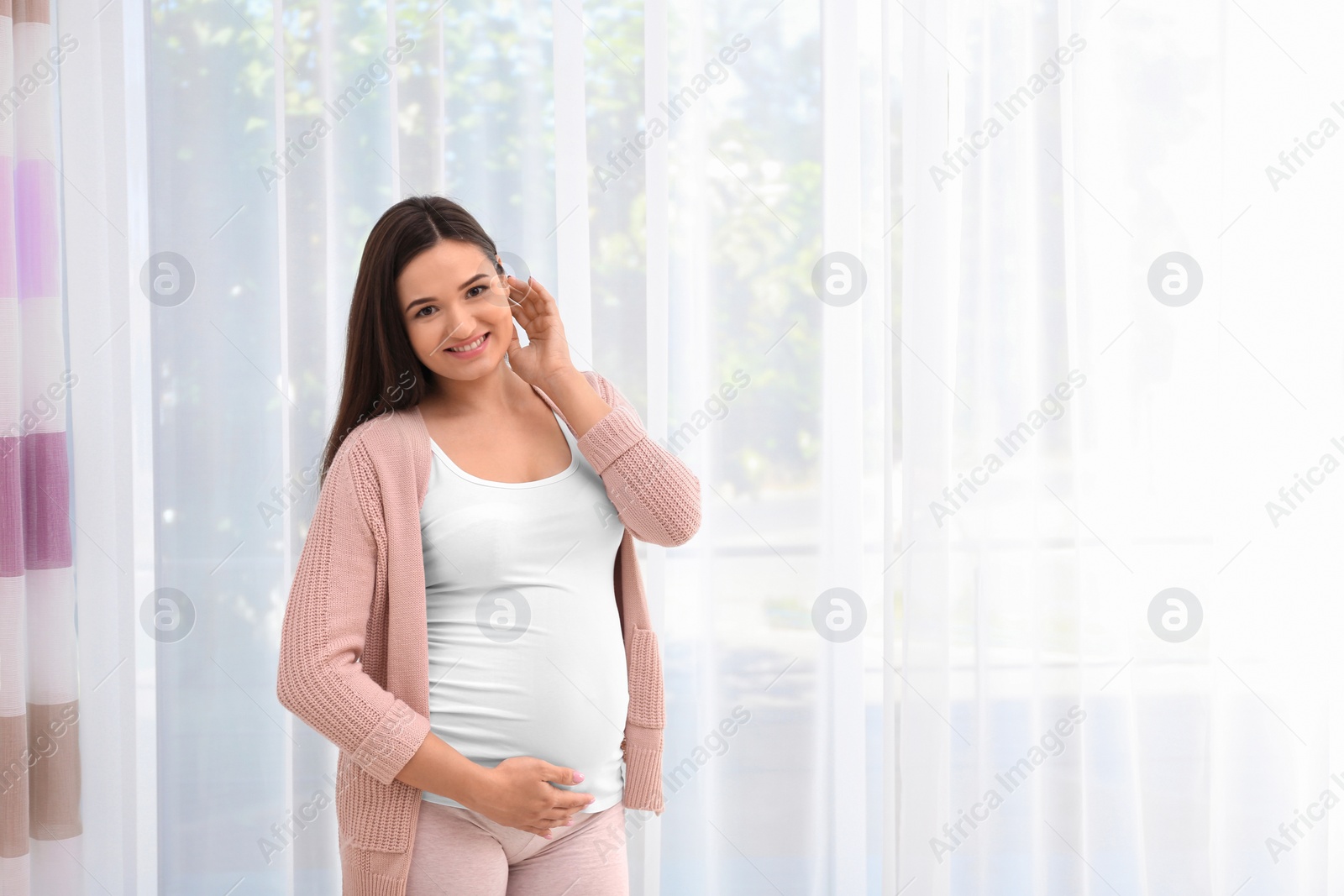 Photo of Young beautiful pregnant woman near window at home