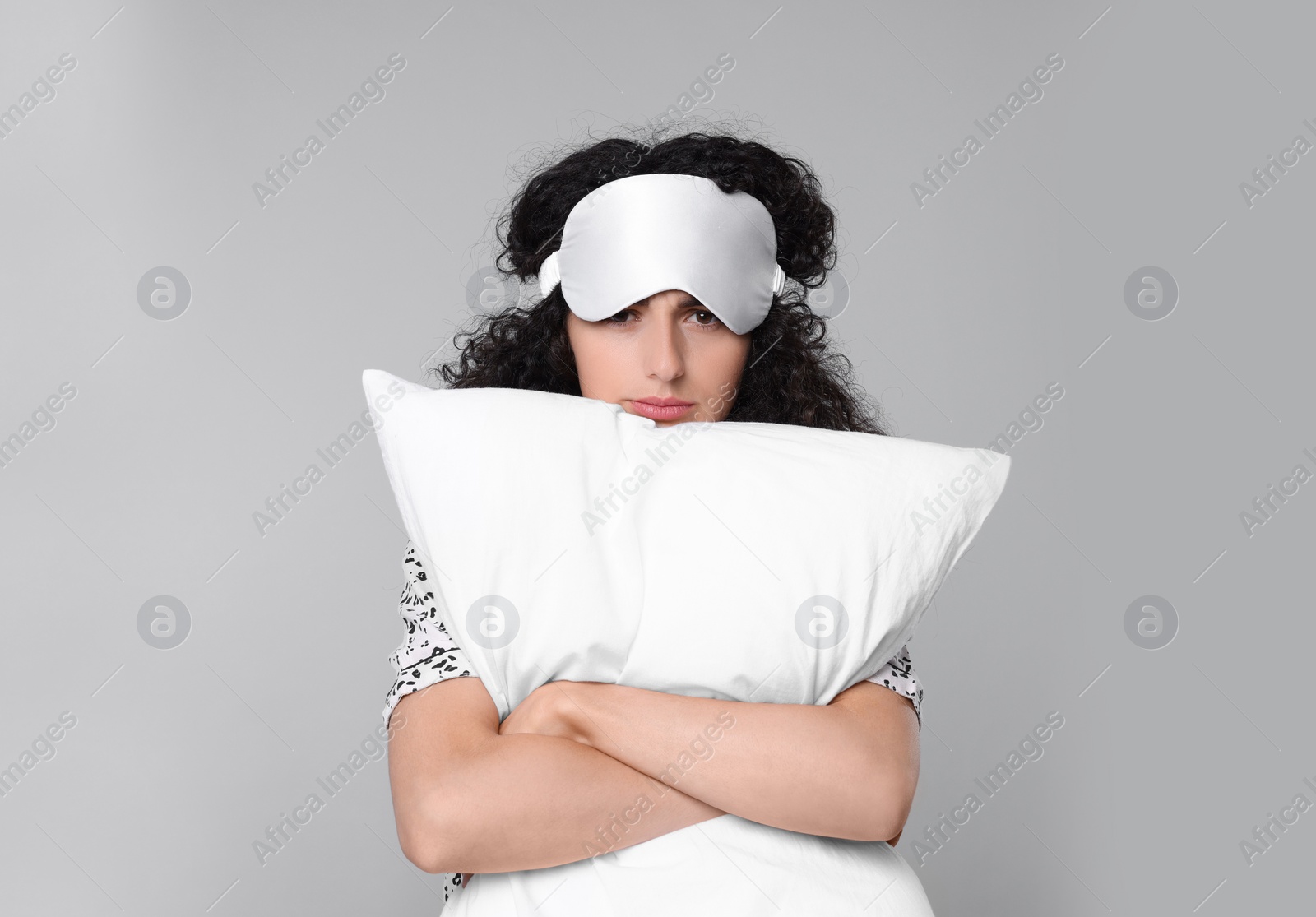 Photo of Tired young woman with sleep mask and pillow on light grey background. Insomnia problem